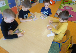 Czterech chłopców siedzi przy stole i składa z części obrazek łąki.